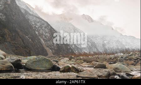 Ein klarer Fluss mit Felsen führt in die Berge, die von der Morgendämmerung beleuchtet werden Stockfoto