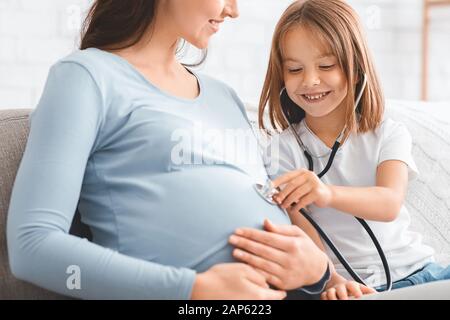 Kleines Mädchen, das mit ihrer schwangeren Mutter einen Arzt spielt Stockfoto
