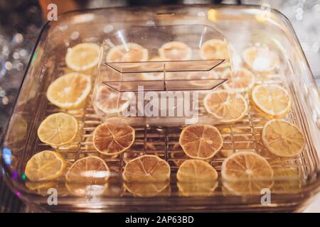 Orangefarbene Scheiben in einer Trocknerflasche auf einem Holztisch. Küchenausstattung zum Trocknen von Obst und Gemüse mit mehreren Regalen Stockfoto
