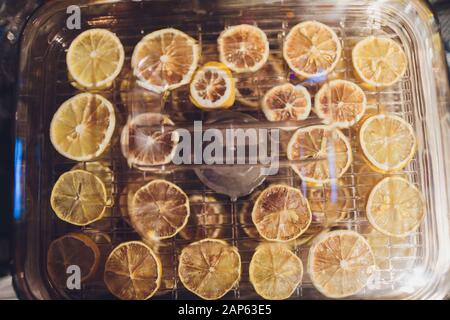 Orangefarbene Scheiben in einer Trocknerflasche auf einem Holztisch. Küchenausstattung zum Trocknen von Obst und Gemüse mit mehreren Regalen Stockfoto