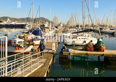 Blick auf den Hafen von Porto Maurizio mit an der Holzpier vermauerten Booten und Fischern an einem sonnigen Wintertag, Imperia, Ligurien, Italien Stockfoto