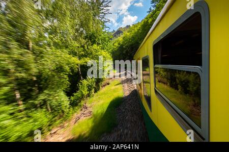 Zugfahrt, Blick aus dem Fenster. Alte Zug passiert grüne Vegetation. Blick aus dem Fenster. Anreise mit der Bahn bis Sonnenuntergang. Sunset Landschaft und ein Zug gil Stockfoto