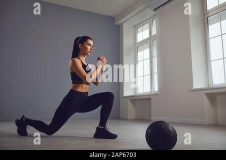 Squat-Übungen. Mädchen in schwarzer Sportkleidung mit Hanteln in den Händen, die in einem Raum hocken. Stockfoto