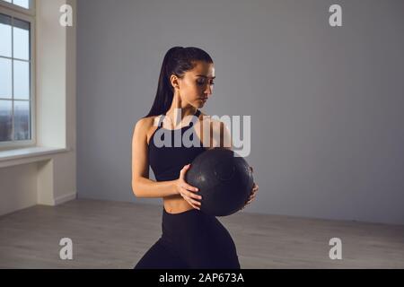 Das Mädchen geht mit einem medizinischen Ball in den Sport. Ein Sportmädchen übt Übungen in einem Raum im Haus aus. Stockfoto