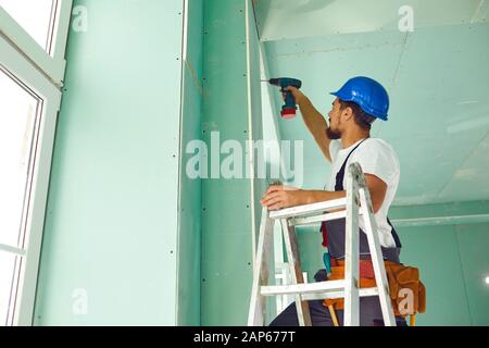 Ein Bauherr auf einer Leiter stehend installiert Trockenbau auf einer Baustelle Stockfoto