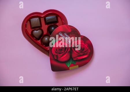 Eine geöffnete, herzförmige Schachtel mit Rosen darauf von Valentinsschokolade in einem Winkel mit pinkfarbenem Hintergrund Stockfoto