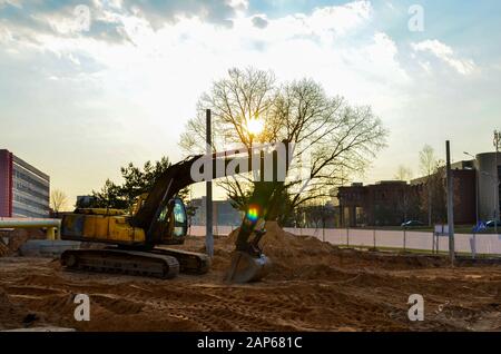 Gelber Bagger auf einer Baustelle während der erdarbeiten und Verlegung von unterirdischen Rohren und Kommunikation in der Stadt, vor dem Hintergrund der Stockfoto