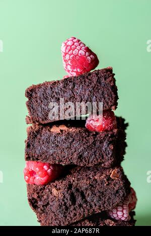 Schokoladenbrownie in einem Stapel mit gefrorenen Beeren auf grünem Hintergrund. Leckere Kakaokuchen. Haufen von Brownies und Himbeeren. Schokoladendessert. Stockfoto