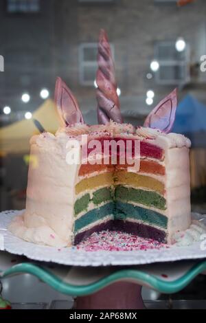 Der mehrfarbige Kuchen in Schichten in Form eines Einhorns in einem Schaufenster. In Stücken verkauft. Stockfoto