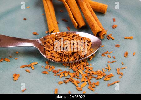 Nahaufnahme eines isolierten Löffels mit zerkleinertem Zimt und Stöcken auf blauem verkratztem china-teller Stockfoto