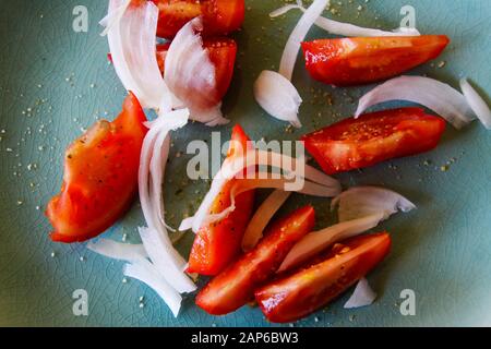 Hochwinkelige Draufsicht Nahaufnahme von frischen rohen roten Tomatenscheiben mit Zwiebeln, gewürzt mit Kräutersalz auf grünem Teller Stockfoto
