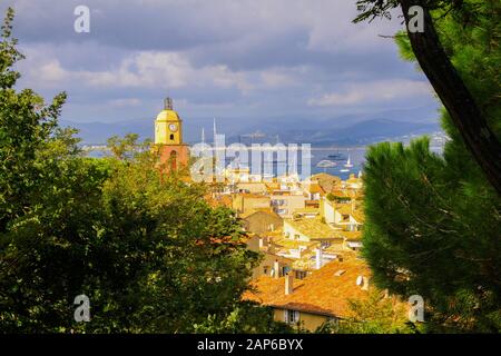Luftbild über die Bäume im mediterranen Dorf mit Kirchturm und Meeresgrund am bewölkten Tag - St. Tropez, Cote d'Azur, Frankreich Stockfoto