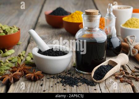 Backkümmel oder römische Koriandersamen, schwarze Carawaj-Ölflaschen und aromatische Gewürze und Kräuter: Kurkuma, Kardamom, Zimt, Nelken, Anis, Paprika. In Stockfoto