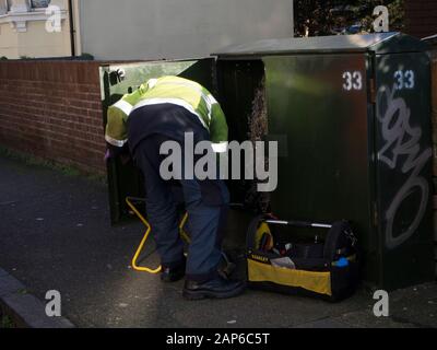 Telekommunikationsingenieur, der an einer grünen Schrankbox in einem Wohngebiet arbeitet Straße Stockfoto