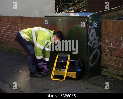 Telekommunikationsingenieur, der an einer grünen Schrankbox in einem Wohngebiet arbeitet Straße Stockfoto