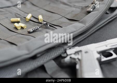 9 mm Kugeln und Pistole liegen auf einem schwarzen taktischen Rucksack. Ein Satz spezieller Dienstgegenstände oder ein Geheimagent. Goldene Schalen verstreut um die Handfeuerwaffe Stockfoto