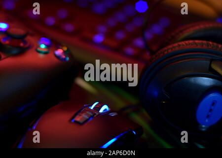 Moderne Gamepad- und Gaming-Maus liegt mit Tastatur und Kopfhörern auf dem Tisch in dunkler Spielraum-Szene in der Nähe. Geräte zum Spielen von Videospielen zu Hause Stockfoto