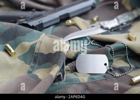 Arme-Dog-Tag-Token mit 9 mm Kugeln und Pistole liegen auf gefaltetem, tarngrünen Stoff. Ein Set von Militärveteranen oder Trophäen-Kit für alte Aufgaben Stockfoto