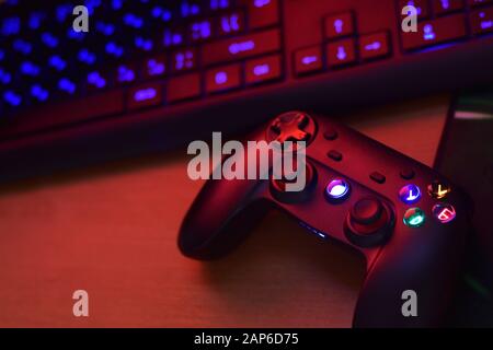 Modernes Gamepad liegt mit pc-Tastatur auf dem Tisch in dunkler Spielraum-Szene in der Nähe. Gameplay-Streaming und Videospiel-Walkthroughts-Konzept Stockfoto