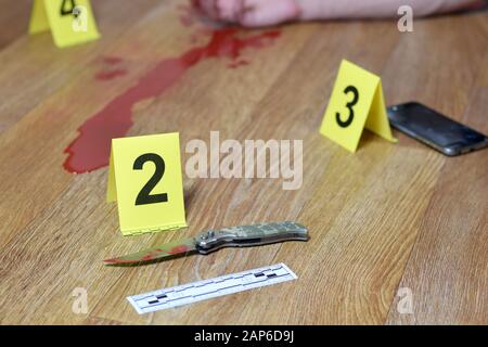 Tatort-Ermittlungen - Blutiges Messer und Opfer reichen mit gelben Strafmarkierungen auf Küchenboden aus. Hinweise auf Tötung Stockfoto