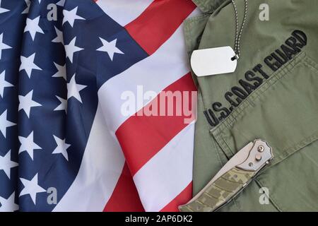 Militärhundekennzeichen und -Messer liegen auf Der Alten Uniform der US Coast Guard und gefalteten Flagge der Vereinigten Staaten. Hintergrund für das Tagesdesign der Küstenwache Stockfoto