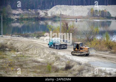 Caterpillar-Lader und Müllkipper arbeiten im Tagebau. Schwere Maschinen im Tagebau am Fluss. Planierraupe und LKW beim Graben und Bagger Stockfoto