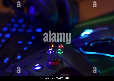Moderne Gamepad- und Gaming-Maus liegt mit Tastatur und Kopfhörern auf dem Tisch in dunkler Spielraum-Szene in der Nähe. Gameplay-Streaming und Videospiel-Walkthro Stockfoto