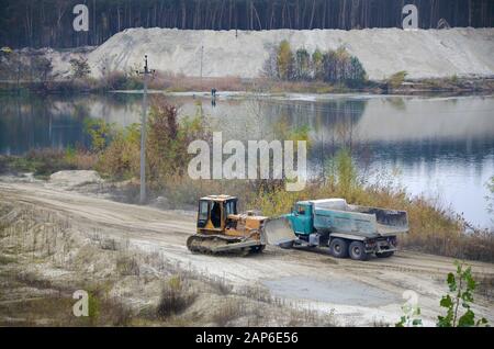 Caterpillar-Lader und Müllkipper arbeiten im Tagebau. Schwere Maschinen im Tagebau am Fluss. Planierraupe und LKW beim Graben und Bagger Stockfoto