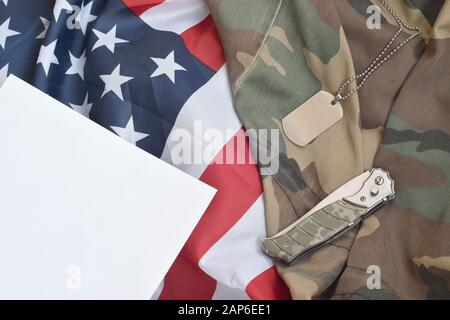 Armee-Hundetag-Token und Messer liegen auf Alter Camouflage-Uniform und gefalteter United States Flag. Hintergrund für Die Gestaltung Des Militärtags Stockfoto