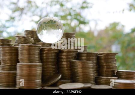 Glasplanet auf einem großen Haufen glänzender ukrainischer alter 1-Hrywnien-Münzstapel dicht oben auf unscharfem grünen Baumhintergrund. Das Konzept des Geldtransfers Stockfoto