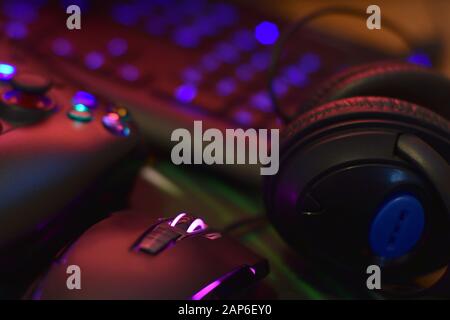 Moderne Gamepad- und Gaming-Maus liegt mit Tastatur und Kopfhörern auf dem Tisch in dunkler Spielraum-Szene in der Nähe. Elektronische Geräte und Technologiekonzept Stockfoto