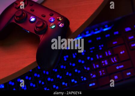Modernes Gamepad liegt mit pc-Tastatur auf dem Tisch in dunkler Spielraum-Szene in der Nähe. Videospiel Speedrun Konzept oder Esports Wettbewerb Herausforderung Stockfoto