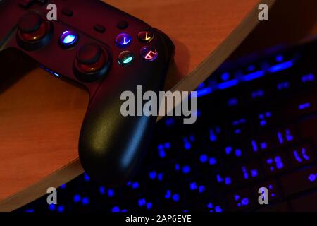 Modernes Gamepad liegt mit pc-Tastatur auf dem Tisch in dunkler Spielraum-Szene in der Nähe. Lassen Sie Videospiele zusammen mit dem Konzept "Freunde" spielen Stockfoto