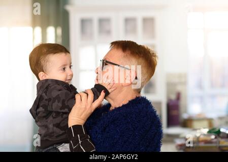 Großmutter hält kleines Kind in den Armen, Baby streichelt Omas Wange. Glückliche Familienmomente. Stockfoto