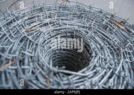 Auf einer Pfahlrolle aus glänzendem, neuem Stacheldraht zum Zaunfechten schließen. Durchsetzung von Sicherheitsvorschriften. Straftat des Gefängnis-Strafvollzugs gesperrt. Stockfoto