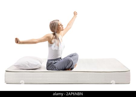 Junge Frau in den Schlafanzügen Sitzen auf einer Matratze und Stretching auf weißem Hintergrund Stockfoto