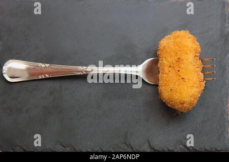 Blick von oben auf eine schwarze Schieferplatte, wo wir eine hausgemachte Krokette auf einer Gabel sehen Stockfoto
