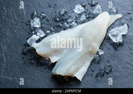 Zwei rohe Walmfilets, Merlangius merlangus, aus einem im Ärmelkanal gefangenen Whiting auf Stab und Linie von einem Boot. Auf Eis und dunklem Schiefer-Backgrod Stockfoto