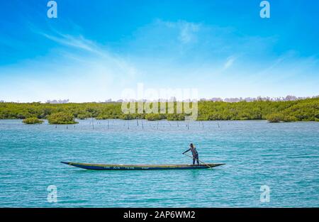 Fadiouth, Senegal, AFRIKA - 26. April 2019: Unidentifizierter senegalesischer Mann fährt mit einem typischen Holzkanu in einer See-Lagune und fischt. Hinter ihm sind es Stockfoto