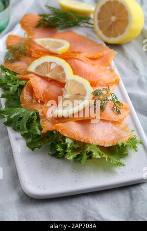 Scheiben geräucherter Lachs mit Salat und in Scheiben geschnittenen Zitrone auf einem Schneidebrett Stockfoto