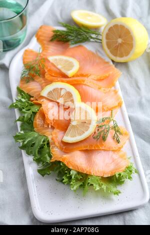 Scheiben geräucherter Lachs mit Salat und in Scheiben geschnittenen Zitrone auf einem Schneidebrett Stockfoto