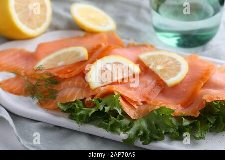 Scheiben geräucherter Lachs mit Salat und in Scheiben geschnittenen Zitrone auf einem Schneidebrett Stockfoto