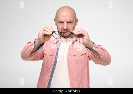 Verärgerter Kahlmann hält Brille in den Händen und untersucht sie alarmiert, er sieht die Ehe auf den Linsen und ist sehr wütend. Stockfoto