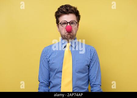 Kaukasischer junger Mann in der roten Clownnase irritiert und traurig. Studio gedreht Stockfoto