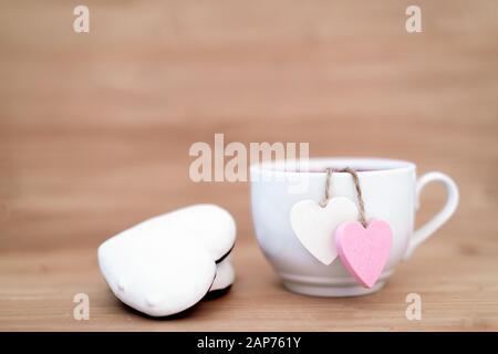 Herzförmige Teebeutel in weißer Tasse Tee mit Ingwerplätzchen - süße Liebeserklärung auf Holzhintergrund, selektiver Fokus. Valentines Tageskonzept. Tasse Tee für zwei Liebhaber Flitterwochen Hochzeit Morgen Überraschung Frühstück Stockfoto