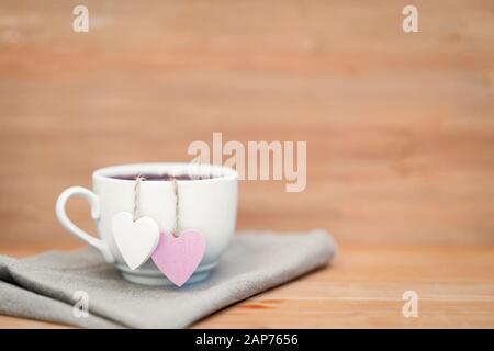 Herzförmige Teetasche in weißer Tasse Tee - süße Liebeserklärung auf Holzhintergrund, selektiver Fokus. Valentines Tageskonzept. Tasse Tee für zwei Liebhaber Flitterwochen Hochzeit Morgen Überraschung Frühstück Stockfoto