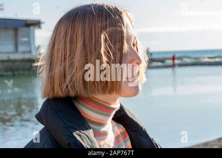 Schönes Teenager-Mädchen mit kurzen Haaren vor dem Hintergrund des Meeres. Urbane Natur, Teenager-Lifestyle Stockfoto