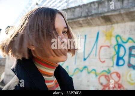 Wunderschönes Mädchen im Teenager-Alter mit kurzen Haaren, die in der Nähe der Graffitiwand pos Urbane Natur, Teenager-Lifestyle Stockfoto