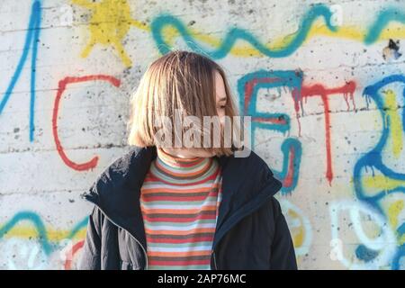 Wunderschönes Mädchen im Teenager-Alter mit kurzen Haaren, die in der Nähe der Graffitiwand pos Urbane Natur, Teenager-Lifestyle Stockfoto