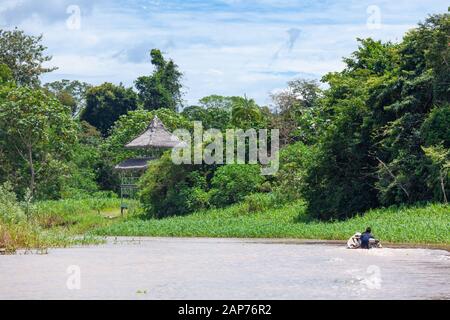 Peru, Amazonas-Fluss - 2019-12-08. Menschen in einem Holzboot eilen zum Haus, schöne Wolken. Stockfoto